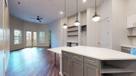 This well-appointed 2-bedroom, 2-bathroom residence offers a thoughtfully designed single-level layout with modern finishes throughout. The open-concept kitchen and living area serves as the heart of the home, anchored by a large center island with a crisp white quartz countertop, gray shaker-style cabinetry with gold hardware, and stylish pendant lighting. The kitchen is equipped with stainless steel appliances including a French door refrigerator, range, microwave, and dishwasher, complemented by a classic subway tile backsplash and a gold-accented faucet. Built-in shelving and a recessed media niche add functional character to the living area, while French doors invite natural light and provide outdoor access. Rich hardwood-style flooring runs throughout the space, lending warmth and continuity. Both bedrooms are well-sized and bright, each featuring natural light from windows with exterior views. The primary bathroom features a walk-in shower with floor-to-ceiling tile, a gray vanity with gold fixtures, and a large framed mirror. The second bathroom offers a soaking tub and shower combination with gold hardware and clean white tile. A dedicated hallway connects all rooms, completing this cohesive and contemporary layout.