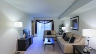 Located at 100 Fox Meadow Drive in Maple Shadow, New Jersey, this single-floor residence offers a thoughtfully designed living environment that balances comfort and functionality. The living room serves as the heart of the home, featuring plush wall-to-wall carpeting that adds warmth underfoot and a soft, neutral color palette throughout the walls and ceiling that creates a calm, inviting atmosphere. A large sliding glass door dressed with elegant floor-to-ceiling vertical blinds and decorative draping floods the space with natural light while providing access to the outdoors. The room offers generous space for seating and entertainment, with a layout that accommodates a full sofa arrangement alongside a media console. Recessed ceiling details add a subtle architectural element, contributing to the clean, structured look of the interior. Accent lighting complements the natural light, enhancing the ambiance during evening hours. The overall design of the home reflects a practical yet refined sensibility, making it a comfortable and well-appointed single-level living space in a residential New Jersey setting.