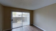 Located at 11355 Zapata in San Diego, this single-story space presents a clean and functional layout with notable architectural details throughout. The main living area features smooth hardwood-style flooring that adds warmth and visual continuity to the space. The textured popcorn ceiling provides a classic finish overhead, while neutral-toned walls create a versatile backdrop suitable for a variety of interior styles.

A standout feature of the living area is the large sliding glass door, framed with vertical blinds that offer adjustable light control. This expansive door draws in ample natural light, brightening the interior and providing views of the surrounding outdoor environment, including neighboring greenery and the exterior landscape. The sliding door also provides direct access to an outdoor area, enhancing the connection between the interior and exterior.

White baseboards frame the perimeter of the room, offering a crisp contrast against the flooring and walls. Overall, the space maintains a straightforward and practical aesthetic, with key features that emphasize natural light, clean finishes, and comfortable livability in a convenient San Diego location.