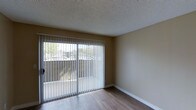 Located at 11355 Zapata in San Diego, this single-story space presents a clean and functional layout with notable architectural details throughout. The main living area features smooth hardwood-style flooring that adds warmth and visual continuity to the space. The textured popcorn ceiling provides a classic finish overhead, while neutral-toned walls create a versatile backdrop suitable for a variety of interior styles.

A standout feature of the living area is the large sliding glass door, framed with vertical blinds that offer adjustable light control. This expansive door draws in ample natural light, brightening the interior and providing views of the surrounding outdoor environment, including neighboring greenery and the exterior landscape. The sliding door also provides direct access to an outdoor area, enhancing the connection between the interior and exterior.

White baseboards frame the perimeter of the room, offering a crisp contrast against the flooring and walls. Overall, the space maintains a straightforward and practical aesthetic, with key features that emphasize natural light, clean finishes, and comfortable livability in a convenient San Diego location.