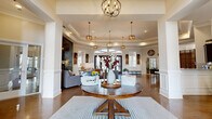 Located at 1709 Cason Ln in Murfreesboro, TN, this elegantly designed single-floor space offers a seamless open-concept layout encompassing a living room, dining area, and kitchen. Polished stained concrete floors flow throughout, complemented by soaring tray ceilings adorned with crown molding and an array of stylish pendant and chandelier lighting fixtures. The welcoming entryway features a glass-paneled door, wainscoting, and generous natural light. The expansive living area centers around a dramatic floor-to-ceiling stacked stone fireplace, paired with warm leather seating, cowhide accents, and arched mirrors that enhance the sense of depth. Large glass entry doors flood the space with abundant natural light and provide views to the outdoors. The kitchen is a standout, boasting dark espresso cabinetry, granite countertops, stainless steel appliances, a stone-accented center island with bar seating, and copper pendant lighting. Decorative columns frame the kitchen and common areas, adding architectural distinction. The dining area accommodates generous gatherings beneath an ornate chandelier. Throughout, the design strikes a balance between rustic warmth and refined elegance, creating an inviting and functional communal atmosphere.