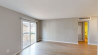 Located at 4305 Hunters Glen Dr in Plainsboro, NJ, this 2-bedroom, 1-bathroom single-floor residence offers a clean, modern aesthetic throughout. Light wood-style flooring runs continuously across all rooms, creating a cohesive and bright atmosphere. The combined kitchen and living area anchors the layout, with the kitchen featuring white shaker cabinetry, granite stone countertops with a stainless undermount sink, a brushed gold faucet, and stainless steel appliances. The living room extends naturally toward a sliding glass door that opens onto a private balcony, allowing natural light to fill the space and providing outdoor views. The primary bedroom is generously sized, offering ample room and a closet for storage. The second bedroom also includes a closet and shares the same warm, neutral tones found throughout the unit. The full bathroom is well-appointed with a white vanity topped with granite countertops, a tub-shower combination with tile surround, and wood-look flooring that ties into the rest of the home. Neutral gray walls throughout give the space a versatile, move-in-ready feel. The entry area includes a closet, adding practical storage at the front door.