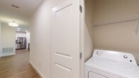 This single-floor residence offers a thoughtfully designed layout that balances functionality and modern style throughout. The open living area serves as the heart of the home, featuring warm hardwood-style flooring, a ceiling fan with light fixture, and generous windows fitted with blinds that invite ample natural light while maintaining privacy. A secondary door provides convenient exterior access directly from the living space.

The kitchen is equipped with stainless steel appliances — including a refrigerator with ice and water dispenser, electric range, and over-the-range microwave — complemented by crisp white shaker-style cabinetry, granite countertops, and matching hardwood-style flooring that ties seamlessly into the living area.

Bedrooms are finished with plush carpeting and feature large windows that bring in natural light and outdoor views, creating a calm and restful atmosphere. The bathroom is finished with consistent granite countertops, a white shaker vanity, a tiled tub-and-shower combination, and hardwood-style flooring — offering a clean, cohesive aesthetic.

An in-unit laundry area with a washer and overhead storage shelving adds practical convenience. Throughout the residence, neutral tones, white trim, and panel-style interior doors contribute to a clean, contemporary feel.
