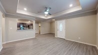 This single-floor unit in Tontitown, Arkansas, presents a well-designed open-concept layout finished with consistent, modern materials throughout. The main living area is defined by a distinctive tray ceiling with crown molding and a ceiling fan with integrated lighting, creating a sense of architectural depth. Wood-look luxury vinyl plank flooring extends throughout the space, providing both durability and visual continuity. A front entry door with an oval glass insert allows natural light into the living area, which also features windows along the front wall.

The kitchen is connected to the living area via an arched passthrough, offering visual openness while maintaining defined spaces. Dark espresso-toned cabinetry with ample upper and lower storage pairs with granite-style countertops and a full suite of stainless steel appliances, including a refrigerator, electric range, over-the-range microwave, and dishwasher.

The bedroom features its own tray ceiling with a ceiling fan and includes access to a walk-in closet with built-in shelving and rod storage. Bathrooms are outfitted with dark vanity cabinetry, granite-style countertops, and tub-shower combinations with clean white surrounds, maintaining the cohesive, contemporary aesthetic found throughout the rest of the unit.