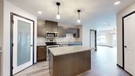 This contemporary single-floor residence offers a thoughtfully designed layout with high-quality finishes throughout. The kitchen serves as the heart of the home, showcasing rich dark wood cabinetry, granite countertops, and a full suite of stainless steel appliances including a refrigerator, electric range, microwave, and dishwasher. A central island with matching granite provides additional prep space and casual seating, while pendant lighting adds a warm, stylish ambiance. A frosted glass interior door adds a modern architectural touch, offering privacy without sacrificing light. The living areas are bright and open, featuring light-toned luxury vinyl plank flooring and large windows that frame views of the surrounding neighborhood. Elevated ceiling details in the main living area lend a sense of spaciousness. The bedrooms are comfortably sized, finished with soft carpet and generous windows that allow natural light to fill the rooms. The bathroom is clean and functional, with a granite-topped vanity with dark wood cabinetry, a tub-shower combination, and matching plank-style flooring that ties together the home's cohesive aesthetic. Neutral wall tones throughout create a versatile, move-in-ready canvas.