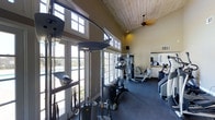 Located at 3402 Calle Odessa in Carlsbad, this fitness center is a well-appointed, single-floor facility designed to support a comprehensive workout experience. The space immediately impresses with its soaring vaulted ceiling clad in warm wood paneling, which lends an inviting, airy feel to the interior. A ceiling fan adds comfort and airflow throughout the room.

Natural light floods the space through a generous arrangement of large, multi-pane French-style doors and transom windows that line the walls, offering views of the outdoors and creating a bright, energizing atmosphere. The dark rubberized flooring provides both safety and durability underfoot.

The facility is outfitted with a diverse selection of cardiovascular and strength-training equipment, including treadmills, elliptical machines, a cable/functional trainer system, a rowing machine, and a stationary bike, among others. A mirrored wall on one side of the room enhances the sense of space and allows users to monitor their form during workouts. A counter area along the mirrored wall offers a convenient space for personal items or equipment accessories.

The combination of architectural character, ample natural light, and well-rounded equipment makes this fitness center a practical and pleasant environment for residents or members seeking an effective and comfortable place to exercise.