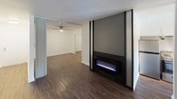 This single-floor space offers a well-designed layout that balances functionality and comfort throughout its interconnected rooms. The main living area is an immediate focal point, highlighted by a striking accent wall finished in dark gray with vertical black trim, housing a sleek electric fireplace that adds a contemporary touch. Wood-look flooring flows throughout the space, creating visual continuity, while a ceiling fan overhead ensures year-round comfort.

Adjacent to the living area, a pass-through breakfast bar connects to the kitchen, which features white cabinetry, light-toned countertops, and a stainless steel range with overhead ventilation hood. A window above the counter allows natural light to enter, with views of the surrounding exterior. The kitchen maintains a clean, efficient design with ample cabinet storage and a stainless steel sink.

Large sliding glass doors fitted with vertical blinds allow generous natural light into the dining and living areas while providing outdoor access. The bathroom is finished in a clean, utilitarian style, featuring a shower-tub combo, toilet, wall-mounted cabinet, and a vanity with a gray countertop. The overall ambiance of the space is bright, neutral, and move-in ready.