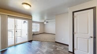 Located at 3230 Champion Dr in Rapid City, South Dakota, this single-floor unit offers a well-organized layout designed for comfortable everyday living. The main living area features durable wood-style flooring that transitions seamlessly into a carpeted lounge space, providing a warm and inviting atmosphere. A ceiling fan overhead and a wall-mounted HVAC unit ensure year-round climate control, while a sliding glass door opens to a private balcony, filling the space with natural light and offering outdoor access. The kitchen is outfitted with rich, dark cabinetry, ample counter space, and a stainless steel refrigerator, complemented by wood-style flooring and pendant lighting that adds a refined touch. The bedroom is generously sized with plush carpeting, a ceiling fan, and a double-door closet for ample storage. Two full bathrooms are present, each featuring a tub-shower combination, dark vanity cabinetry, light-toned tile flooring, and clean white fixtures. Textured ceilings and dark trim accents throughout the unit provide a cohesive, polished aesthetic. The layout flows efficiently from room to room, making practical use of the available space.