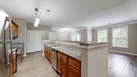Located at 8931 N Rhode Ave in Kansas City, MO, this single-floor, two-bedroom, two-bathroom residence offers a well-organized layout with a cohesive, neutral design aesthetic throughout. The open-concept kitchen and living area serves as the heart of the home, where warm honey-toned cabinetry pairs with granite countertops and stainless steel appliances, including a refrigerator, range, and dishwasher. A peninsula counter with pendant lighting provides additional workspace and separates the kitchen from the living area, which features crown molding, wood-style flooring, and multiple windows that invite natural light. The primary bedroom is a comfortable retreat with plush carpeting, a ceiling fan, and direct access to an en-suite bathroom featuring a double granite-topped vanity, a glass-enclosed shower, and a soaking tub. A spacious walk-in closet with wire shelving and hanging rods provides generous storage. The second bedroom also features carpeting, a ceiling fan, and natural light from dual windows. The second bathroom offers a granite vanity, wood-style flooring, and a glass-enclosed shower. Additional features include a dedicated laundry area and hallways connecting all areas of the home efficiently.