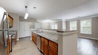 Located at 8931 N Rhode Ave in Kansas City, MO, this single-floor, two-bedroom, two-bathroom residence offers a well-organized layout with a cohesive, neutral design aesthetic throughout. The open-concept kitchen and living area serves as the heart of the home, where warm honey-toned cabinetry pairs with granite countertops and stainless steel appliances, including a refrigerator, range, and dishwasher. A peninsula counter with pendant lighting provides additional workspace and separates the kitchen from the living area, which features crown molding, wood-style flooring, and multiple windows that invite natural light. The primary bedroom is a comfortable retreat with plush carpeting, a ceiling fan, and direct access to an en-suite bathroom featuring a double granite-topped vanity, a glass-enclosed shower, and a soaking tub. A spacious walk-in closet with wire shelving and hanging rods provides generous storage. The second bedroom also features carpeting, a ceiling fan, and natural light from dual windows. The second bathroom offers a granite vanity, wood-style flooring, and a glass-enclosed shower. Additional features include a dedicated laundry area and hallways connecting all areas of the home efficiently.
