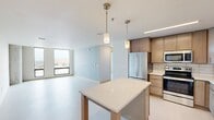 Located at 215 S Pinckney St in the heart of downtown Madison, Wisconsin, this well-appointed one-bedroom, one-bathroom residence offers a thoughtfully designed layout with contemporary finishes throughout. The open-concept kitchen and living area serves as the centerpiece of the home, featuring light wood cabinetry, stainless steel appliances, a subway tile backsplash, and a striking quartz-topped island with pendant lighting — ideal for both cooking and casual dining. The kitchen flows seamlessly into the living space, creating a bright and functional common area with light-toned flooring that runs throughout the unit. The bedroom is a comfortable, well-proportioned retreat highlighted by large floor-to-ceiling windows that frame impressive views of the Madison skyline. A distinctive curved concrete column adds an architectural character unique to the space, while a ceiling fan contributes to year-round comfort. The full bathroom is cleanly designed with a quartz vanity countertop, a full soaking tub with shower, and modern fixtures. A dedicated closet provides practical storage. The unit's light, neutral palette and modern design elements combine to create a calm, urban living environment in one of Madison's most vibrant downtown locations.