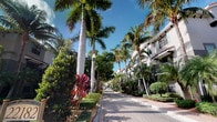 This single-floor property is situated within a beautifully maintained tropical community that immediately impresses with its lush, resort-style surroundings. The exterior environment is defined by towering royal palms and a rich variety of tropical foliage, including colorful ornamental plants that line a well-kept brick-paved walkway. The pedestrian pathway creates a welcoming approach, shaded by a canopy of mature palm trees that evoke a warm, coastal ambiance. Neighboring structures feature a classic white stucco architectural style with balconies and clean lines, consistent with South Florida's Mediterranean-influenced design tradition. The grounds are meticulously landscaped with trimmed hedges, ground cover, and accent plantings that add layers of color and texture throughout the common areas. Street lamps along the walkway provide a sense of security and charm, enhancing the community's polished aesthetic both day and night. The overall atmosphere is one of serene, tropical living set within a well-appointed residential community, offering a tranquil environment just steps from the front door. The combination of lush greenery, elegant architecture, and thoughtfully designed outdoor spaces makes this property an inviting and visually appealing place to call home.