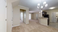 This single-story residence offers a well-organized, open-concept layout designed for comfortable everyday living. The main living area is generously proportioned, featuring plush wall-to-wall carpeting, crown molding, and a tiled fireplace with built-in shelving. A large sliding glass door floods the space with natural light and provides outdoor views, enhancing the bright, airy atmosphere throughout.

The kitchen is a functional highlight, showcasing dark espresso cabinetry, granite-patterned countertops, and a full suite of black appliances including a refrigerator, range, dishwasher, and built-in microwave. A peninsula with pendant lighting and a granite countertop creates a seamless transition into the dining and living areas. A dedicated laundry area with a full-size washer and dryer is conveniently accessible directly from the kitchen.

The bedrooms are carpeted and well-lit by windows with exterior greenery views, offering a calm and private retreat. The bathrooms feature neutral tile flooring, white subway tile tub surrounds, and dark vanity cabinetry with light countertops, maintaining a consistent and cohesive design palette. A hallway with closet access connects the private areas of the home efficiently. Overall, the space presents a clean, neutral aesthetic suitable for a variety of interior styles.