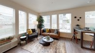 This single-floor residence offers a thoughtfully designed layout with a contemporary aesthetic carried consistently throughout each space. The open-concept kitchen serves as a central hub, featuring white shaker cabinetry, quartz countertops, a large center island with seating, stainless steel appliances, subway tile backsplash, and pendant lighting — all set atop durable wood-look flooring.

The living area is well-lit by a bank of large windows fitted with white blinds, allowing generous natural light while offering views of the surrounding neighborhood. Wood-look flooring continues here, complementing the neutral, warm-toned walls.

Two bedrooms provide comfortable retreats, each with carpeted floors, multiple windows, and ample natural light. A versatile den or office space accommodates a dedicated work area, complete with carpet and a window overlooking the exterior.

Two bathrooms serve the residence: one featuring a soaking tub and shower combination with a white vanity and quartz countertop, and a second with a standalone glass-enclosed shower, a gray vanity, and wood-look flooring. Both bathrooms maintain a clean, modern finish consistent with the overall design of the space.