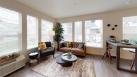 This single-floor residence offers a thoughtfully designed layout with a contemporary aesthetic carried consistently throughout each space. The open-concept kitchen serves as a central hub, featuring white shaker cabinetry, quartz countertops, a large center island with seating, stainless steel appliances, subway tile backsplash, and pendant lighting — all set atop durable wood-look flooring.

The living area is well-lit by a bank of large windows fitted with white blinds, allowing generous natural light while offering views of the surrounding neighborhood. Wood-look flooring continues here, complementing the neutral, warm-toned walls.

Two bedrooms provide comfortable retreats, each with carpeted floors, multiple windows, and ample natural light. A versatile den or office space accommodates a dedicated work area, complete with carpet and a window overlooking the exterior.

Two bathrooms serve the residence: one featuring a soaking tub and shower combination with a white vanity and quartz countertop, and a second with a standalone glass-enclosed shower, a gray vanity, and wood-look flooring. Both bathrooms maintain a clean, modern finish consistent with the overall design of the space.