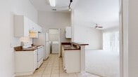 This well-appointed single-floor residence features 2 bedrooms and 2 bathrooms within a thoughtfully designed open-concept layout. The kitchen serves as a functional hub, outfitted with white cabinetry, a peninsula with a dark countertop and sink, white appliances including a refrigerator and electric range, and track lighting overhead. It opens seamlessly into the living area, which features vaulted ceilings, plush carpeting, a ceiling fan, and expansive sliding glass doors flanked by a large window that bathe the space in natural light and provide access to the outdoors. The primary bedroom is generously sized, showcasing vaulted ceilings, a large window with outdoor views, and a walk-in closet with wire shelving. The second bedroom also features vaulted ceilings, soft carpeting, and a window that allows natural light to flow in. Both bathrooms are finished with tile flooring, white vanity cabinetry, large mirrors, and well-lit fixtures; one features a shower-tub combination. A dedicated in-unit laundry room accommodates a full-sized washer and dryer side by side with overhead shelving. The hallway connects all rooms efficiently, completing this practical and comfortable single-level layout.