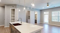 This two-story home offers a clean, modern aesthetic throughout its two bedrooms, two bathrooms, and well-organized layout across two floors. The main level features an open-concept kitchen and living area bathed in natural light from large windows. The kitchen is outfitted with gray shaker-style cabinetry, stainless steel appliances including a refrigerator with ice and water dispenser, a microwave, and a range, all complemented by white quartz countertops and a stylish tile backsplash. A generous island with pendant lighting serves as the centerpiece, ideal for both meal prep and casual dining. The living room features light hardwood-style flooring, recessed lighting, and a ceiling fan. A dedicated laundry room with washer and dryer hookups adds everyday convenience, while the attached garage provides secure parking and additional storage. Upstairs, the primary bedroom is generously sized with plush carpeting, a ceiling fan, and a walk-in closet. The bathrooms are finished with marble-style tile surrounds, gray cabinetry, and brushed nickel fixtures. Three closets throughout the home ensure ample storage. Neutral gray tones and contemporary finishes give the entire space a cohesive, move-in-ready feel.