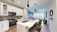 Located at 550 Stanton in Frederick, Maryland, this well-appointed 2-bedroom, 2-bathroom residence offers a thoughtfully designed open-concept layout across a single floor. The kitchen is a standout centerpiece, featuring white shaker cabinetry with glass-front uppers, a gray subway tile backsplash, stainless steel appliances, and a large island with a built-in sink and bar seating — all illuminated by dramatic black pendant lighting. The kitchen flows seamlessly into the dining area, which benefits from large windows and direct access to an exterior door, and further into the living room, where oversized windows, sheer drapery, and a ceiling fan create a bright, airy atmosphere. Wood-look flooring runs throughout the entire home, lending warmth and continuity. The primary bedroom is a comfortable retreat with a large window and direct access to an en-suite bathroom, which includes a white vanity, walk-in glass shower with subway tile, and a connected closet. The second bedroom offers similar natural light and easy access to a full second bathroom featuring a tub-shower combo with subway tile and a matching white vanity. Clean neutral tones and modern finishes define the overall aesthetic of this residence.