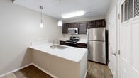 Located at 550 Harbor Cove Ln in Charleston, SC, this well-appointed one-bedroom, one-bathroom home offers a practical and comfortable single-floor layout. The kitchen serves as a functional centerpiece, featuring a peninsula with a white countertop and undermount sink, dark espresso cabinetry, stainless steel appliances including a refrigerator, range, and microwave, and pendant lighting overhead — all set atop durable wood-look flooring. The open design allows for easy flow between the kitchen and living areas. The bedroom is a comfortably sized retreat finished with soft wall-to-wall carpeting, neutral gray walls, a ceiling fan with lighting, and a window that frames views of lush greenery, filling the room with natural light. A dedicated closet provides convenient storage directly off the bedroom. The bathroom is clean and functional, outfitted with wood-look flooring, a dark vanity with a white countertop and framed mirror, and a full tub-shower combination. A hallway connects the rooms seamlessly, completing the efficient and cohesive floor plan. The overall aesthetic is neutral and move-in ready, with consistent finishes throughout.
