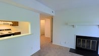 Located at 1142 Harbour Dr in Wilmington, North Carolina, this single-floor residence offers a straightforward and functional layout designed for comfortable everyday living. The main living area is finished with wall-to-wall carpeting and bright white walls that create a clean, neutral backdrop throughout the space. A fireplace anchors one side of the living room, adding a warm and inviting focal point to the area. A pass-through window connects the kitchen to the living space, enhancing the open feel and making the layout well-suited for both everyday use and entertaining. Overhead, a structural beam adds a subtle architectural detail to the ceiling, which also features a centrally placed HVAC vent for climate control. A hallway leads from the main living area to additional rooms beyond, offering a sense of depth and privacy within the floor plan. The interior is uniformly lit with warm ambient lighting, contributing to an inviting atmosphere throughout. The space presents a clean, move-in ready canvas with practical features and a cohesive design suited to a variety of living arrangements.