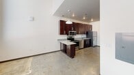 This two-floor loft in Burlington, NC blends industrial and modern design. The main level features polished concrete floors and an open-concept kitchen equipped with rich dark-wood cabinetry, granite countertops, stainless steel appliances, a peninsula with pendant lighting, and a convenient half bath. The upper mezzanine level showcases warm hardwood floors, a dramatic vaulted ceiling with exposed white-paneled sloping walls, visible steel beams, and exposed ductwork. A full bathroom with granite vanity and tub-shower combo completes the upper floor. Natural light enters through a window on the upper level, enhancing the open, airy ambiance throughout.