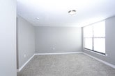 This single-floor unit offers a practical and straightforward layout, as seen in the overhead floor plan view. The living area is generously proportioned, finished with neutral-toned wall-to-wall carpeting and painted in soft greige tones that contribute to a calm, understated ambiance. A wall-mounted HVAC unit provides direct climate control, and horizontal blinds on the windows allow for adjustable natural light throughout the space. Flush-mount ceiling light fixtures provide consistent overhead illumination.

A secondary carpeted room, visible through an open doorway, offers additional flexible living or sleeping space. Both rooms feature clean white baseboards and multiple electrical outlets positioned conveniently along the walls.

The kitchen area, as shown in the floor plan, is compact yet functional, equipped with a white refrigerator and a freestanding electric range. Cabinetry and countertop space provide essential storage and prep areas, while tile flooring distinguishes the kitchen zone from the carpeted living spaces.

The bathroom features a full tub and shower combination, with floor-to-ceiling earth-toned tile surrounding the fixture. Brushed nickel hardware and a towel bar add a cohesive, modern finish to the space.