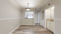 This single-floor residence offers a thoughtfully designed layout with a cohesive, neutral aesthetic carried throughout every room. Durable wood-look plank flooring flows seamlessly across the entire space, complementing the warm, light gray tones of the walls and crisp white trim work. The living area is enhanced by elegant crown molding and a large sliding glass door that invites abundant natural light and outdoor views. An entry foyer opens naturally into the living space, where a pendant light fixture adds a refined touch. The adjacent dining area features a decorative pendant light and a pass-through window connecting directly to the kitchen, creating an open, communicative feel between the spaces. Built-in shelving provides convenient storage along one wall of the dining area. The kitchen is equipped with white cabinetry, granite-style countertops, a stainless steel double sink, a dishwasher, and a warm mosaic tile backsplash in earth tones. The bedrooms are generously sized, each with natural light from windows with blinds, ceiling fans, and closet access. The bathroom features a clean, white tub-shower combination, a vanity with a granite-style countertop, and matching wood-look flooring. Overall, the space presents a clean, move-in-ready atmosphere with practical finishes throughout.