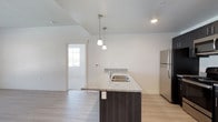 This single-floor residence offers a clean, contemporary design with a cohesive neutral palette throughout. The kitchen serves as a central highlight, featuring a large island with granite countertops and an integrated stainless steel sink, complemented by elegant pendant lighting overhead. Dark espresso cabinetry contrasts beautifully against the light countertops, while a full suite of stainless steel appliances — including a refrigerator, range, microwave, and dishwasher — adds a polished, functional edge. Light wood-style flooring runs through the kitchen and living areas, contributing to a bright and airy atmosphere.

The living area is generously proportioned, with natural light streaming in through large windows and a neutral color scheme that enhances the sense of openness. Bedrooms are carpeted for comfort and each feature windows with outdoor views, providing a calm and restful setting.

Two full bathrooms mirror each other in style, each outfitted with granite-topped dark vanities, tub-shower combinations with curved curtain rods, and light wood-style flooring. The consistent use of quality finishes and neutral tones across all rooms creates a cohesive, move-in-ready living environment that is both practical and visually appealing.
