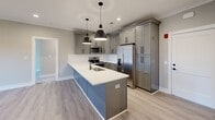 This single-story home in Lynchburg, Virginia offers a cohesive, modern aesthetic defined by neutral tones, clean lines, and quality finishes throughout. The kitchen serves as a standout centerpiece, featuring gray shaker-style cabinetry, a striking blue island with a white quartz countertop, stainless steel appliances, a classic white subway tile backsplash, and matte black pendant lighting. Light wood-look flooring flows through the main living and kitchen areas, lending warmth and continuity to the open layout.

The living area is bright and airy, enhanced by crown molding, recessed lighting, a ceiling fan, and French doors that invite natural light and provide outdoor access. Multiple carpeted bedrooms offer a comfortable feel, each equipped with ceiling fans and windows fitted with horizontal blinds for light control and privacy. The rooms are finished with clean white baseboards against soft gray walls, creating a calm, neutral environment.

The bathroom is well-appointed with a dual-sink vanity featuring gray cabinetry, chrome hardware, white quartz countertops, a large mirror with wall sconces, and marble-look tile flooring. Overall, the home presents a clean, move-in-ready interior with consistent, contemporary detailing.