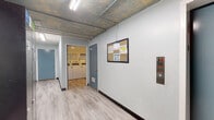 Located at 5447 White Oak Ave in Encino, California, this single-floor common area facility offers a range of practical amenities within a distinctively designed interior. The hallway is the visual centerpiece of the space, featuring a striking hand-painted underwater mural that spans the length of the corridor. The artwork depicts marine life including a shark, fish, and lush seagrass rendered across exposed concrete block walls, creating an immersive and memorable aesthetic. Light wood-style flooring runs throughout, complementing the industrial-style exposed ceiling with fluorescent strip lighting and visible utility conduits. The corridor provides access to multiple areas, including a dedicated locker room equipped with tall dark metal lockers with electronic locks, continuing the ocean mural theme. A bulletin board and fire safety panel are conveniently positioned near the elevator, which offers accessible floor navigation. The shared laundry room is well-appointed with multiple top-load washing machines, a dryer, and a folding counter, all maintained in a clean, bright environment with recessed lighting and posted operating instructions. This facility combines functional amenities with creative design, making it a well-equipped and visually engaging shared space.