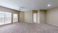 This single-floor residence features a cohesive design characterized by warm beige walls, plush neutral-toned carpeting, and white trim throughout. The living area is generously sized, benefiting from natural light streaming through large windows with blinds, and is equipped with a ceiling fan for added comfort. A door provides direct access to the outdoors, enhancing the connection to the exterior. Multiple additional rooms, also carpeted and bathed in neutral tones, offer flexible use as bedrooms or private spaces, each featuring ceiling fans or overhead lighting and ample wall space. The kitchen is designed with dark espresso-toned cabinetry, granite-style countertops, hardwood-style flooring, black appliances including an electric range and dishwasher, and a pantry closet, creating a practical and attractive cooking environment. The bathroom continues the dark cabinetry theme, featuring a granite-style vanity countertop, overhead cabinetry for storage, wood-style flooring, a large mirror, and a shower-tub combination. A hallway connects the bedroom to the bathroom, providing a convenient layout. Overall, the space presents a clean, functional, and cohesive aesthetic.