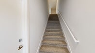 This two-story space is designed with a clean, contemporary aesthetic that carries consistently throughout both levels. The carpeted staircase, framed by crisp white walls and a sleek handrail, connects the floors and sets a neutral, modern tone from the outset.

The kitchen features light hardwood flooring, gray shaker-style cabinetry with brushed hardware, white quartz countertops, and a stainless steel refrigerator. The bright, airy color palette creates an open and functional atmosphere. Adjacent living areas continue the light hardwood flooring and are illuminated by recessed lighting and ceiling fans, with windows offering views of surrounding greenery.

Bedrooms are carpeted in neutral tones and include ceiling fans, natural light from windows with blinds, and access to closet space. The bathrooms are finished to a high standard, featuring gray vanity cabinetry, white quartz countertops, LED-lit mirrors, matte black fixtures, large-format wall tile, and light hardwood flooring. One bathroom includes a tub-shower combination, while another offers a glass-enclosed shower. The overall ambiance is bright, clean, and move-in ready.