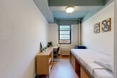 Located at 419 W 34th Street in the heart of Midtown Manhattan, this private room offers a well-organized and functional living space designed to maximize every square foot. The room features light wood flooring throughout, which complements the clean white walls and a distinctive teal-painted ceiling detail that adds a subtle touch of character to the space.

The bedroom is efficiently furnished with a platform bed that includes built-in drawer storage underneath, making excellent use of the compact footprint. Along the opposite wall, a natural wood built-in desk and shelving unit provide a dedicated workspace, complete with a desk chair — ideal for studying or remote work. A wall-mounted mirror and small potted plants add a personal, lived-in feel to the room.

Natural light enters through a window fitted with blinds and a wall-mounted air conditioning unit, while a classic cast-iron radiator beneath ensures warmth during cooler months. A wall-mounted sink is conveniently located near the entry door, alongside open shelving that serves as the closet area for hanging and storing belongings. Overhead, a flush-mount ceiling light provides functional illumination throughout the room.

Situated steps from Penn Station and Madison Square Garden, this room offers a practical and comfortable base in one of New York City's most connected neighborhoods.