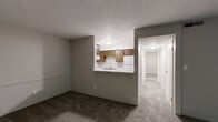 This two-bedroom, three-bathroom unit at 900 Long Blvd in Lansing, Michigan offers a practical and well-organized single-floor layout. The combined living and dining area is carpeted and bathed in natural light, with a sliding glass door opening onto a private balcony with outdoor views of surrounding greenery. A pass-through counter connects the living area to the kitchen, which features warm wood-toned cabinetry, white appliances including an electric range and dishwasher, light countertops, and easy-care hard-surface flooring. A dedicated hallway leads to both bedrooms, each finished with soft carpet and windows fitted with blinds that bring in natural light. The spacious primary bedroom includes a generous walk-in closet with built-in shelving and hanging rods. Three closets throughout the unit provide ample storage. The bathrooms are clean and functional, with at least one featuring a tub-shower combination, a floating vanity with a single sink, and hard-surface flooring. Textured ceilings are consistent throughout the unit. The overall layout is efficient and functional, making good use of the available floor space to provide comfortable living accommodations in a residential Lansing neighborhood.