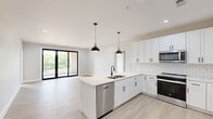 This well-appointed 2-bedroom, 2-bathroom single-floor residence offers a thoughtfully designed open-concept layout that seamlessly connects the kitchen and living room. The kitchen is a standout feature, showcasing white shaker cabinetry with matte black hardware, a classic subway tile backsplash, a central island with a double sink and pendant lighting in a black-and-gold finish, and stainless steel appliances. Light hardwood-style flooring flows throughout the entire unit, enhancing the bright, airy atmosphere. The living area is generously proportioned and opens directly to a private balcony through sleek black-framed sliding glass doors, filling the space with natural light and offering pleasant outdoor views. Both bedrooms are well-sized, with the primary bedroom providing direct access to the balcony and featuring a ceiling fan and abundant natural light. The primary bedroom is accompanied by a spacious walk-in closet outfitted with multi-tier shelving and black hanging rods. The bathrooms are finished with white vanities, matte black fixtures, round mirrors, and elegant penny tile flooring. A dedicated laundry room with a full-size Whirlpool washer and dryer adds everyday convenience. Three closets total provide ample storage throughout the unit.