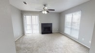 This single-story residence offers a practical and comfortable layout across two bedrooms and one bathroom. The living room serves as the centerpiece of the home, featuring a dark tile-surround fireplace as a focal point, soft carpeted flooring, and a ceiling fan with integrated lighting. Natural light enters through a large window fitted with horizontal blinds, while a sliding glass door with vertical blinds provides direct access to an outdoor area. The textured ceiling adds a traditional finish throughout the living spaces.

The kitchen is equipped with black appliances, including a top-freezer refrigerator and range, alongside a stainless steel sink, light-toned countertops, and gray cabinetry. Hard surface flooring in the kitchen provides a practical contrast to the carpeted areas elsewhere. The bedrooms are carpeted and bright, each featuring ceiling fans and multiple windows with blinds that allow for ample natural light and ventilation. The bathroom is finished with large-format gray tile in the shower surround, a light stone-toned vanity countertop with an integrated sink, and a framed mirror above. The overall color palette throughout the home features neutral gray tones on the walls, creating a cohesive and move-in ready environment.