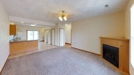 This single-story home offers a practical and comfortable layout throughout. The living area features plush carpeting, a ceiling fan with light fixture, and a fireplace with a wood-trimmed surround, creating a warm focal point. The space flows openly toward the kitchen and dining area, which transitions to tile flooring. The kitchen is well-equipped with warm oak cabinetry, granite-look countertops, and white appliances including a range, dishwasher, microwave, and refrigerator. A sliding glass door in the kitchen/dining area provides direct access to the outdoors and brings in natural views of the surrounding greenery.

The bedrooms are carpeted and feature ceiling fans, warm wood baseboards, and ample natural light from double windows. One bedroom includes two side-by-side closets, offering generous storage. A teal front entry door welcomes guests into the main living space.

Two full bathrooms serve the home, each featuring tile flooring, a tub/shower combination, a wood-trimmed vanity with a single sink, and a large mirror. One bathroom features warm yellow walls and wainscoting-style tile accenting. Overall, the home maintains a clean, neutral palette with consistent warm wood trim details throughout.
