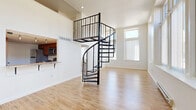 Located at 500 Tripoli Street in Pittsburgh's North Side, this two-bedroom, three-bathroom home spans two floors and offers a thoughtfully designed layout with standout architectural details. The main level features a spacious open-plan living and dining area bathed in natural light from large windows with vertical blinds, all set atop warm hardwood-style flooring. A dramatic black spiral staircase serves as the focal centerpiece, rising to a mezzanine-level upper floor. The kitchen is well-appointed with rich wood cabinetry, stone-patterned countertops, and stainless steel appliances, with a convenient pass-through connecting it to the living space. Three full bathrooms are distributed across the home, including one with a full soaking tub and shower combo with clean white finishes and wood-tone flooring. The bedrooms offer generous proportions, plush carpeting, high ceilings, and abundant natural light through tall windows. The primary bedroom includes built-in closet space and an adjoining vanity area. Additional features include multiple closets, a utility room, and hallways that contribute to the home's practical flow. The bright, neutral palette throughout creates a clean and airy ambiance.