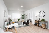 This single-floor residence is thoughtfully designed with a modern, neutral aesthetic throughout. The open-concept kitchen serves as a central highlight, featuring white shaker cabinetry, quartz countertops, a large central island with seating for multiple bar stools, pendant lighting, and a full suite of stainless steel appliances including a refrigerator, range, and microwave. Light wood-look flooring runs through the kitchen and connects seamlessly to the adjacent living and dining areas.

The living room is well-proportioned and bright, benefiting from natural light through large windows with white blinds. A private entry door with sidelights adds direct accessibility to this area.

The unit includes multiple bedrooms, each carpeted for comfort. The primary bedroom is generously sized with a large window, while the secondary bedrooms offer comfortable dimensions suited for varied uses. A tray ceiling detail is featured in one bedroom, adding architectural interest.

The bathroom is finished with light wood-look flooring, white cabinetry with brushed nickel hardware, and a clean, spacious layout. A hallway connects the main living areas to the bedrooms and provides access to additional storage, contributing to the overall functional flow of the space.