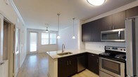 This single-floor, one-bedroom, one-bathroom unit offers a functional and modern open-concept layout that seamlessly connects the kitchen and living area. The kitchen serves as the centerpiece of the space, featuring dark espresso cabinetry that contrasts elegantly with light granite countertops. A peninsula island with an undermount sink provides additional prep space and casual seating potential, while pendant lighting above adds a stylish, contemporary touch. Stainless steel appliances, including a range, microwave, and dishwasher, complete the kitchen's polished look. A classic white subway tile backsplash ties the design together. The living area extends naturally from the kitchen, bathed in natural light from large windows with horizontal blinds. Light-toned hardwood-style flooring runs throughout, contributing to a warm and cohesive aesthetic. A ceiling fan in the living space adds both comfort and functionality. The overall ambiance is clean, modern, and efficiently designed, making excellent use of the available space while maintaining a bright and welcoming atmosphere throughout.