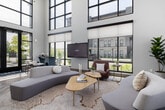 Located in Meridian, Idaho, this thoughtfully designed lobby offers a welcoming and sophisticated first impression. The space is defined by its dramatic double-height ceilings and expansive floor-to-ceiling windows that flood the interior with abundant natural light while framing views of the surrounding outdoor amenities, including a pool area. A herringbone-patterned hardwood floor runs throughout, adding warmth and texture to the contemporary aesthetic.

The central lounge area serves as the heart of the lobby, furnished with curved sectional sofas, accent chairs in rich jewel tones, and organic-shaped coffee tables arranged atop a patterned area rug — creating an inviting gathering space. A large mounted display screen is positioned for easy viewing from the seating area.

The reception zone features a striking marble-faced desk alongside a streamlined wood service counter, both backed by the dramatic window wall overlooking the outdoor space. A modern sputnik-style chandelier adds an artistic focal point overhead.

Flanking the lounge, a bold topographic line-art mural stretches across a full accent wall, rising to the full height of the space and lending the lobby a distinctive, design-forward identity. Glass-enclosed private offices and hallways extend from this feature wall, offering functional spaces that maintain visual connectivity with the main lobby. The overall ambiance is polished, bright, and contemporary.