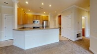 Located at 1300 Deemers Landing in New Castle, Delaware, this generously sized single-floor residence offers two bedrooms, two bathrooms, and a thoughtfully designed layout that maximizes comfort and functionality. The open-concept kitchen and living area serves as the heart of the home, featuring warm honey-toned cabinetry, stainless steel appliances including a refrigerator, range, and microwave, granite-style countertops, recessed lighting, and a central island that seamlessly connects the kitchen to the carpeted living space. Crown molding and classic wainscoting add refined architectural character throughout.

The spacious living room is bathed in natural light through large sliding glass doors and windows, and is accented by a ceiling fan and direct access to an outdoor balcony. Both bedrooms are well-proportioned, carpeted, and feature bright windows with views of surrounding greenery. The primary bedroom is notably generous in size and includes crown molding details. A dedicated walk-in closet with built-in wire shelving and hanging rods provides ample organized storage.

The bathrooms are finished with neutral ceramic tile flooring, a tub-shower combination, and warm wood vanity cabinetry. The overall aesthetic is clean, bright, and move-in ready, offering a comfortable and practical living environment.