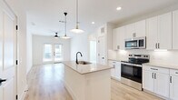 Located in McKinney, TX, this well-designed 2-bedroom, 2-bathroom single-story home offers a clean, modern aesthetic with thoughtful finishes throughout. The open-concept kitchen and living area serves as the heart of the home, anchored by a central kitchen island with a quartz countertop, undermount sink, and matte black faucet. White shaker-style cabinetry, stainless steel appliances — including a French door refrigerator, range, and microwave — complement the light wood-look flooring that flows throughout the main living areas. Stylish pendant lights with brass accents illuminate the kitchen, while a ceiling fan keeps the living room comfortable. French doors in the living area invite natural light and provide access to the outdoors. Both bedrooms feature plush carpeting, ceiling fans, and windows with outdoor views, offering a quiet retreat. Each bedroom is served by its own closet, including a walk-in closet with built-in shelving and hanging rods. The bathrooms are finished with quartz-topped vanities, white cabinetry, matte black hardware, and tile-surround tub and shower combinations. A hallway connects the private areas of the home, completing a functional and cohesive layout.