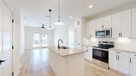 Located in McKinney, TX, this well-designed 2-bedroom, 2-bathroom single-story home offers a clean, modern aesthetic with thoughtful finishes throughout. The open-concept kitchen and living area serves as the heart of the home, anchored by a central kitchen island with a quartz countertop, undermount sink, and matte black faucet. White shaker-style cabinetry, stainless steel appliances — including a French door refrigerator, range, and microwave — complement the light wood-look flooring that flows throughout the main living areas. Stylish pendant lights with brass accents illuminate the kitchen, while a ceiling fan keeps the living room comfortable. French doors in the living area invite natural light and provide access to the outdoors. Both bedrooms feature plush carpeting, ceiling fans, and windows with outdoor views, offering a quiet retreat. Each bedroom is served by its own closet, including a walk-in closet with built-in shelving and hanging rods. The bathrooms are finished with quartz-topped vanities, white cabinetry, matte black hardware, and tile-surround tub and shower combinations. A hallway connects the private areas of the home, completing a functional and cohesive layout.