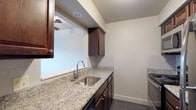 Located at 360 Broad Meadows Blvd in Columbus, Ohio, this single-floor unit offers a thoughtfully updated interior with a cohesive design throughout. The kitchen is a standout feature, showcasing granite countertops with subtle veining, rich dark-stained cabinetry, a stainless steel undermount sink, and stainless steel appliances. A pass-through window connects the kitchen to the living area, enhancing the open feel of the space. The living room is generously sized, featuring dark hardwood-style flooring, a ceiling fan with light fixture, and a window that allows natural light to fill the room. The bedroom continues the same flooring aesthetic and includes a closet with built-in shelving, offering practical storage. The bathroom is well-appointed with a full tub and shower combination, a dark-stained vanity with a white countertop, a large mirror, and gray tile accents on the walls and floor. Throughout the unit, neutral wall tones, textured ceilings, and consistent dark flooring create a clean, modern ambiance. The efficient floor plan connects all areas seamlessly, making this a comfortable and functional living space.