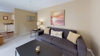 This single-floor residence is thoughtfully laid out to maximize functionality across its key living spaces. The living room features plush carpeting, warm beige walls, and ample room for seating and a workspace, creating a versatile area suitable for both relaxing and working from home. Natural light filters through the space, complementing the neutral color palette.

The kitchen is equipped with white cabinetry, dark countertops, and white appliances, including a range and refrigerator. Wood-look flooring adds warmth and flows into the adjacent dining area, which benefits from multiple windows that bring in natural light and views of the surrounding greenery. The dining space comfortably accommodates a full-sized table and chairs.

The primary bedroom is generously sized with soft carpeting, a large window, and room for a full dresser and nightstands. A second bedroom, also carpeted and windowed, offers a comfortable and adaptable space. Two bathrooms serve the residence — one featuring a walk-in shower with wood-look flooring, and the other with a full soaking tub, an extended vanity, and matching wood-look floors. Throughout, the warm beige tones and consistent finishes create a cohesive and inviting atmosphere.