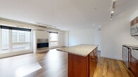 This two-story home offers a well-organized layout across two floors, with the majority of the common living space on the main level and the bedrooms situated above. The main floor is anchored by a generous open-concept kitchen and living room combination. The living area features warm hardwood flooring, a sleek modern fireplace framed by a large window that invites natural light, and track lighting overhead. The kitchen is outfitted with rich wood cabinetry, granite countertops, a mosaic tile backsplash, and stainless steel appliances including a range and built-in microwave. A substantial kitchen island with a granite surface provides additional workspace and casual seating. A dedicated laundry room on the main level houses a stacked washer and dryer unit with tile flooring. The upper floor accommodates three bedrooms, each carpeted for comfort. The bedrooms feature neutral tones and built-in closet storage, with one room offering a walk-in closet with wire shelving beneath a sloped ceiling. The single full bathroom includes a granite-topped vanity with wood cabinetry, a tub-shower combination, and tile flooring, presenting a clean and functional finish throughout.
