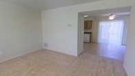This two-floor residence offers a practical and functional layout designed to maximize living comfort. The main level presents an open-concept design where the living room flows seamlessly into the dining and kitchen areas. The living room features neutral wall-to-wall carpeting and light-toned walls that create a clean, airy atmosphere. A floor vent and wall thermostat are conveniently integrated into the living space, ensuring climate control throughout.

An open archway connects the living room to the adjacent kitchen and dining area, where the flooring transitions to tile. The kitchen is equipped with wood-toned cabinetry, dark countertops, and a white range, offering a functional cooking environment. Overhead lighting illuminates the kitchen workspace effectively.

The dining area benefits from abundant natural light streaming through a large window dressed with vertical blinds, enhancing the brightness of the space. The overall color palette throughout the main level is neutral and understated, lending a versatile backdrop suitable for a variety of interior styles. With its straightforward layout and multi-floor design, this residence provides a well-organized living environment that balances practicality with comfortable, everyday functionality.