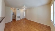 This single-story space offers a clean, functional layout designed for comfortable everyday living. The main living area is open and well-lit, featuring warm wood-look flooring that extends throughout the common spaces. A ceiling fan overhead provides air circulation, while multiple windows fitted with blinds allow natural light to fill the room. A front entry door with a sidelight panel leads directly into this space, which flows seamlessly toward a dining area separated by a half-wall with a countertop pass-through.

The galley-style kitchen runs along a narrow corridor and is equipped with dark wood cabinetry, dark countertops, a white electric range, over-the-range microwave, refrigerator, and a double sink. The kitchen connects conveniently to the rest of the unit via a central hallway.

Both bedrooms feature plush carpeting, ceiling fans with light fixtures, and windows that bring in natural light. Each room includes closet access, with one bedroom offering a spacious reach-in closet with bifold doors.

Two full bathrooms serve the unit, each featuring a tub-shower combination, toilet, and wood-look flooring. One bathroom includes a dark wood vanity with a single sink and a large mirror, while the other offers a windowed wall for added brightness. Overall, the space maintains a neutral, light palette throughout.