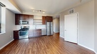 Located at 811 S Washington Ave in Minneapolis, MN, this 2-bedroom, 1-bathroom unit offers a well-organized layout across a single floor. The kitchen is a standout feature, showcasing rich dark wood cabinetry, open shelving, a white subway tile backsplash, light countertops, and a full suite of stainless steel appliances including a gas range, microwave, dishwasher, and refrigerator. Warm hardwood-style flooring extends through the kitchen and main living area, complemented by track lighting overhead. Both bedrooms are carpeted and finished in neutral tones, providing a calm and comfortable atmosphere. The primary bedroom features a ceiling fan and ample space, while the second bedroom includes a window with city views and an exposed concrete structural column, adding an urban, industrial character to the room. Closet space is well-appointed, with double doors in the primary bedroom offering generous storage. The bathroom is finished with classic white subway tile surrounding a full bathtub and shower, paired with dark floor tile for a clean, timeless aesthetic. Natural light enters through multiple windows throughout the unit, offering views of the surrounding Minneapolis cityscape.